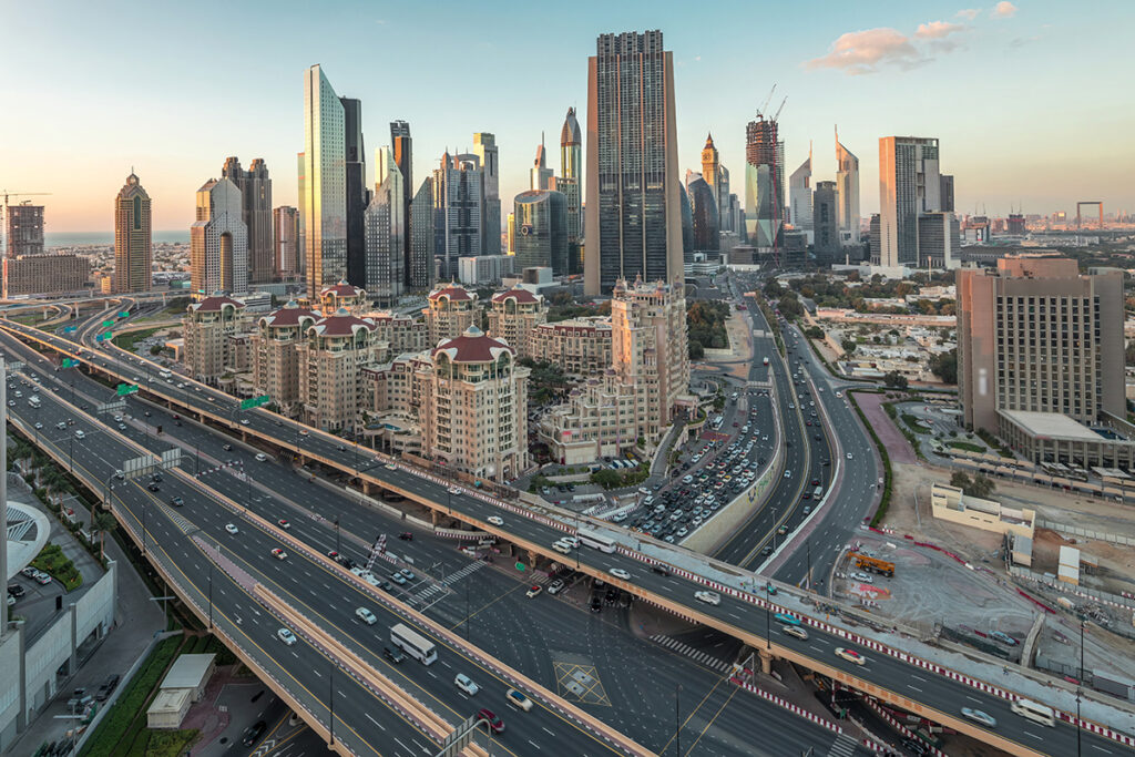Aerial view of Dubai’s modern skyline with high-rise towers, highways, and residential buildings at sunset.